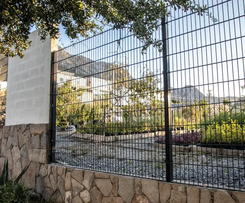 Reja Contemporánea DEACERO negra montada sobre muro de piedra en un desarrollo con áreas verdes