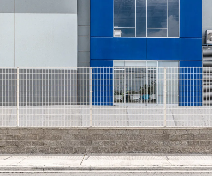 Reja Contemporánea DEACERO en blanco delimitando una nave industrial de fachada azul
